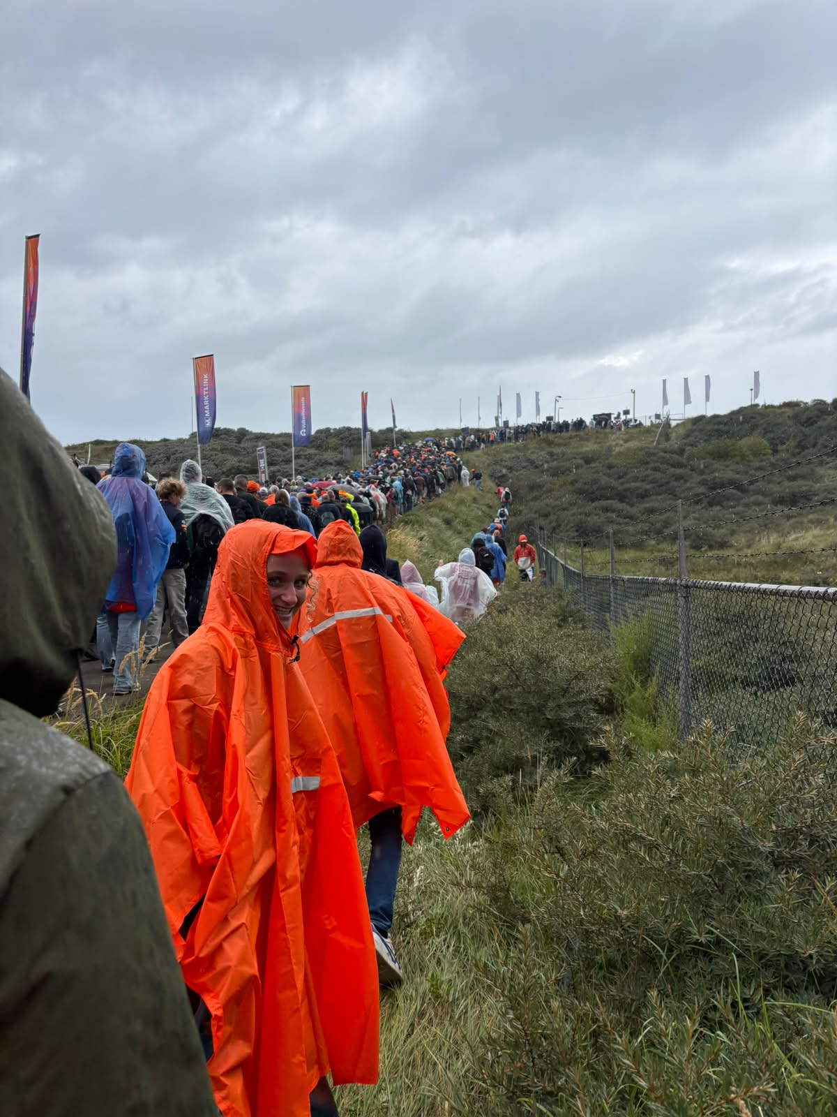 A racegoer in an orange poncho on a wet path through the dunes